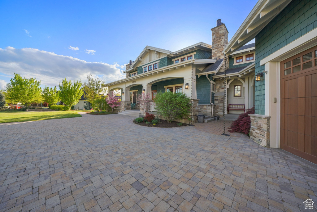 Craftsman-style home with a porch, curved driveway, a chimney, and stone siding