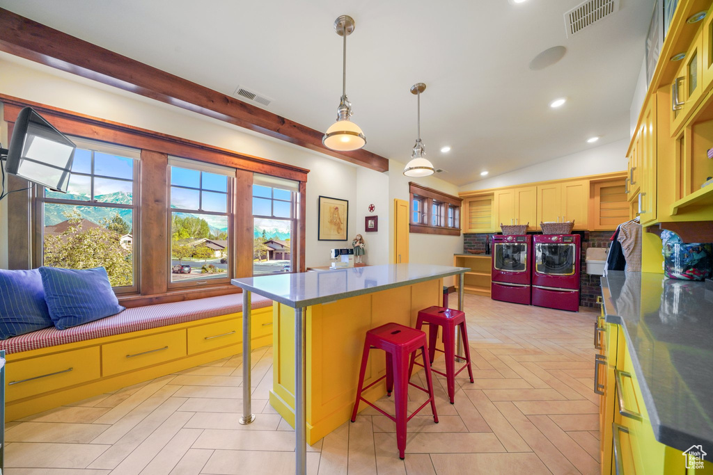 Kitchen featuring washing machine and clothes dryer, dark countertops, visible vents, and a breakfast bar