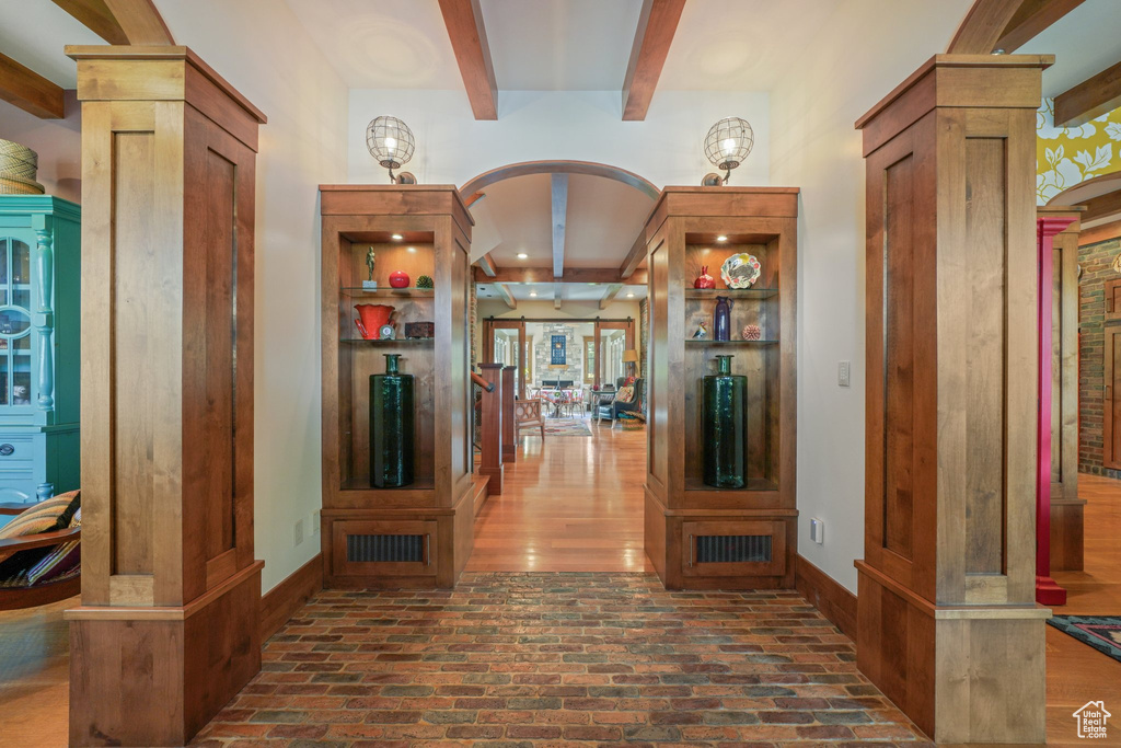 Corridor featuring beamed ceiling, brick floors, arched walkways, decorative columns, and baseboards