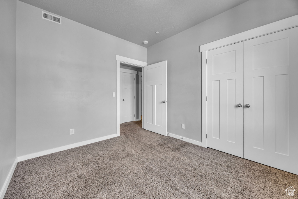 Unfurnished bedroom with carpet floors, baseboards, visible vents, and a closet