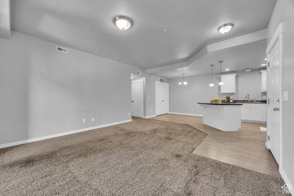 Unfurnished living room featuring light colored carpet, light wood-style flooring, baseboards, and visible vents