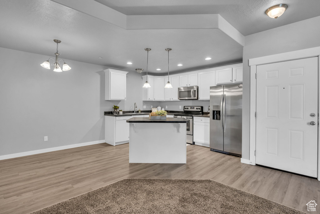 Kitchen with a sink, light wood-style flooring, baseboards, dark countertops, and appliances with stainless steel finishes