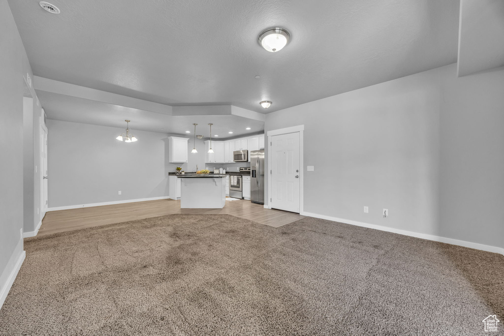 Unfurnished living room with an inviting chandelier, light carpet, and baseboards
