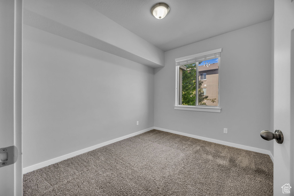 Carpeted spare room featuring lofted ceiling and baseboards