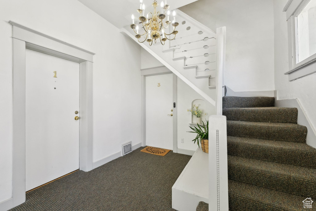 Carpeted foyer entrance with stairway, a notable chandelier, and visible vents