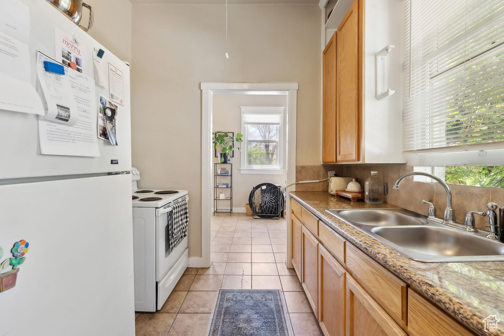 Kitchen featuring a sink, light tile patterned flooring, white appliances, and baseboards