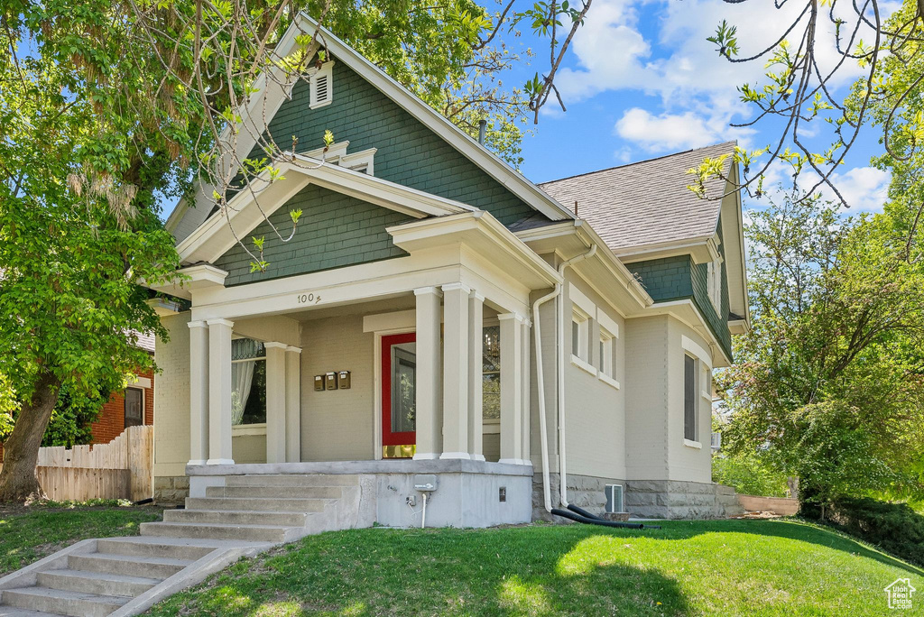 View of front of home with a porch, fence, brick siding, a front lawn, and a shingled roof
