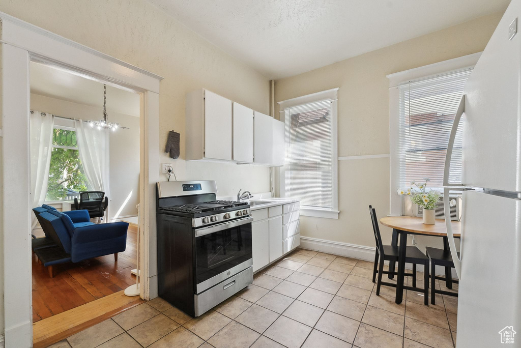 Kitchen with stainless steel range with gas stovetop, freestanding refrigerator, white cabinetry, and a sink
