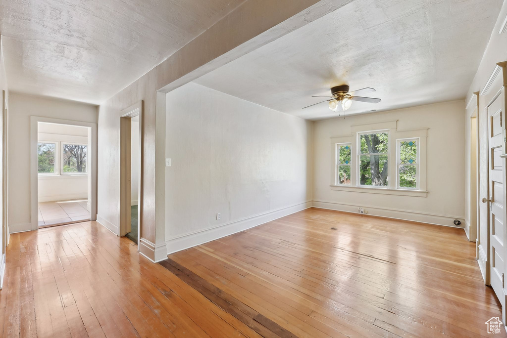 Empty room featuring baseboards, light wood finished floors, a healthy amount of sunlight, and ceiling fan