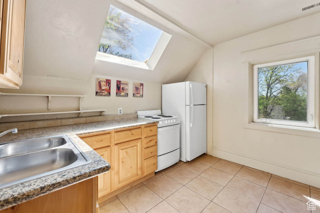 Kitchen featuring lofted ceiling with skylight, a sink, light brown cabinets, visible vents, and white appliances