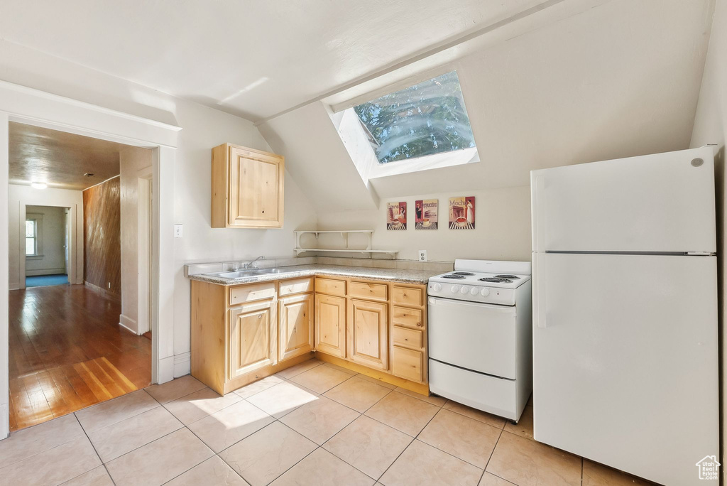 Kitchen featuring light countertops, light brown cabinets, and white appliances