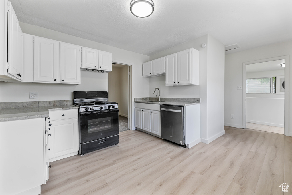 Kitchen with a sink, dishwasher, light wood finished floors, black gas range, and white cabinets