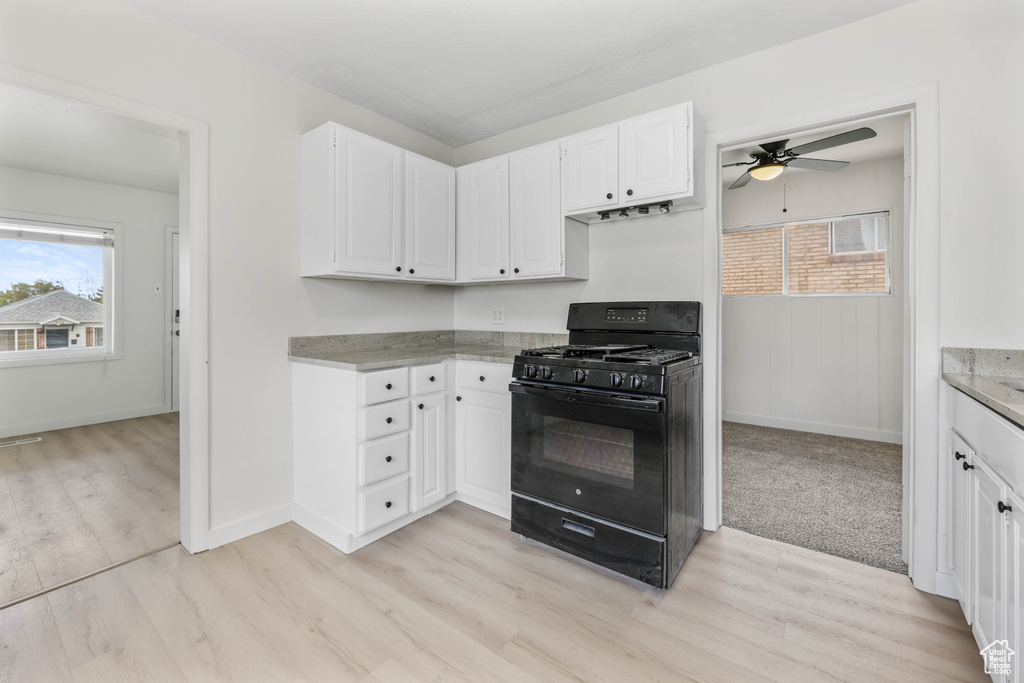Kitchen featuring a ceiling fan, baseboards, white cabinetry, black gas range, and light wood-type flooring