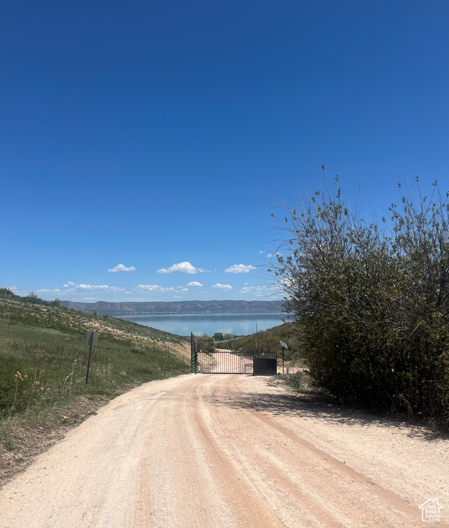 View of dirt / gravel driveway with a gate, a water view, and a gated entry