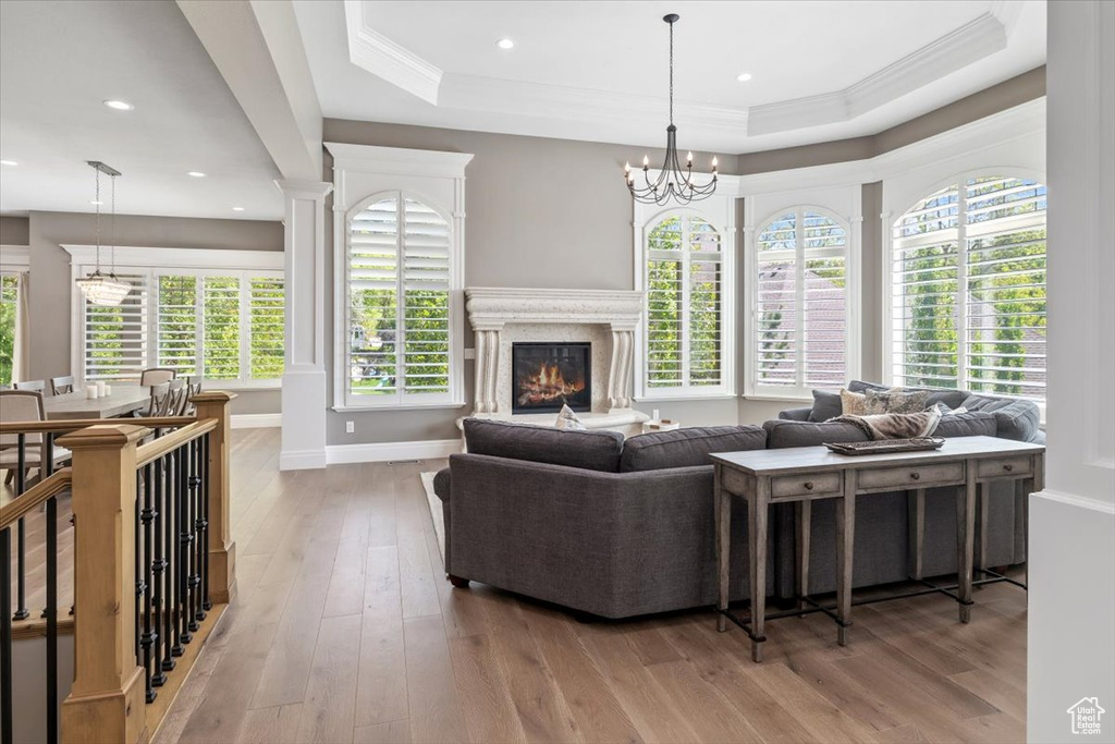 Living area with a tray ceiling, a fireplace, hardwood / wood-style floors, a notable chandelier, and baseboards