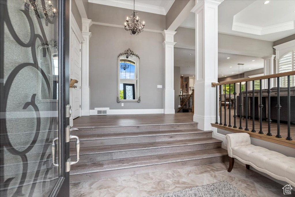 Entrance foyer featuring visible vents, decorative columns, a chandelier, crown molding, and stairway