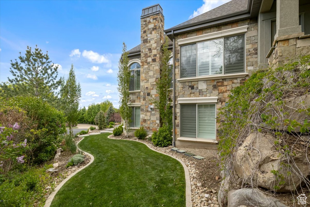 View of home\'s exterior featuring a lawn, stone siding, roof with shingles, and a chimney