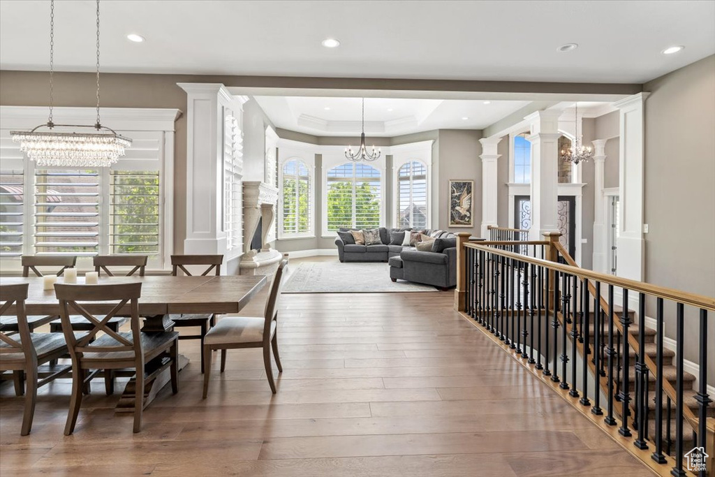 Dining space with an inviting chandelier, ornate columns, a tray ceiling, hardwood / wood-style flooring, and recessed lighting