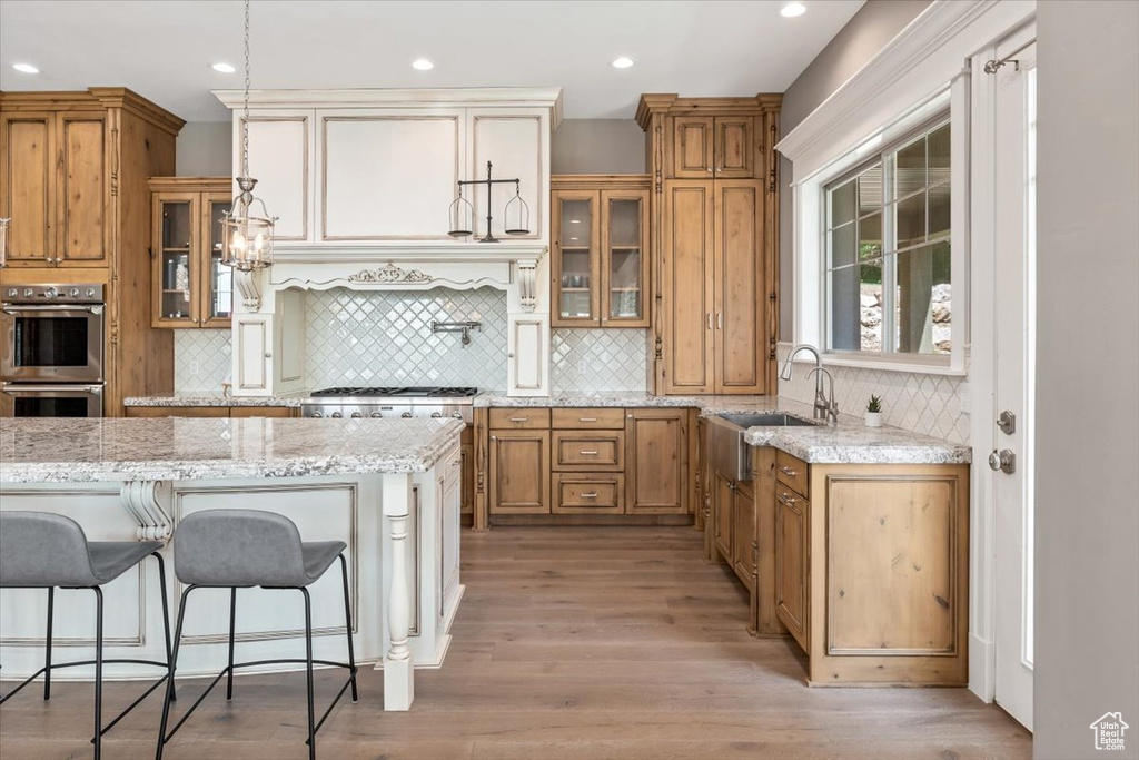 Kitchen featuring glass insert cabinets, light wood finished floors, a sink, stainless steel appliances, and tasteful backsplash
