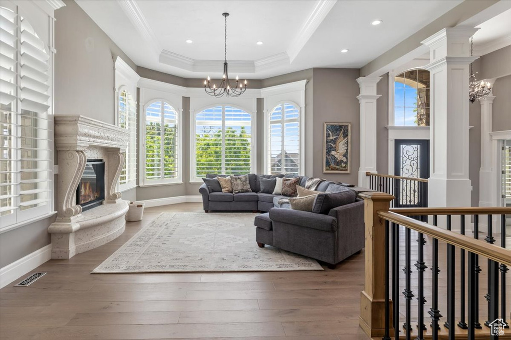 Living room featuring a raised ceiling, a notable chandelier, a fireplace, and wood finished floors