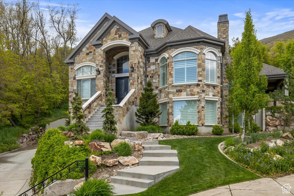 French country home with stone siding, a chimney, and a front yard