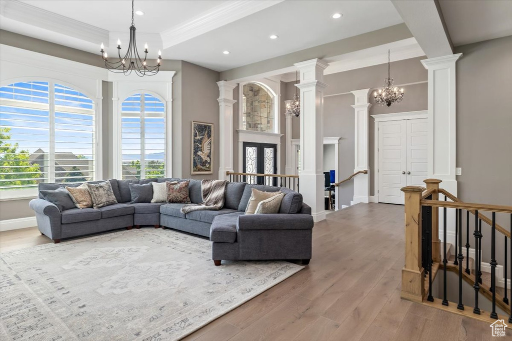 Living area featuring wood finished floors, ornate columns, a notable chandelier, crown molding, and recessed lighting
