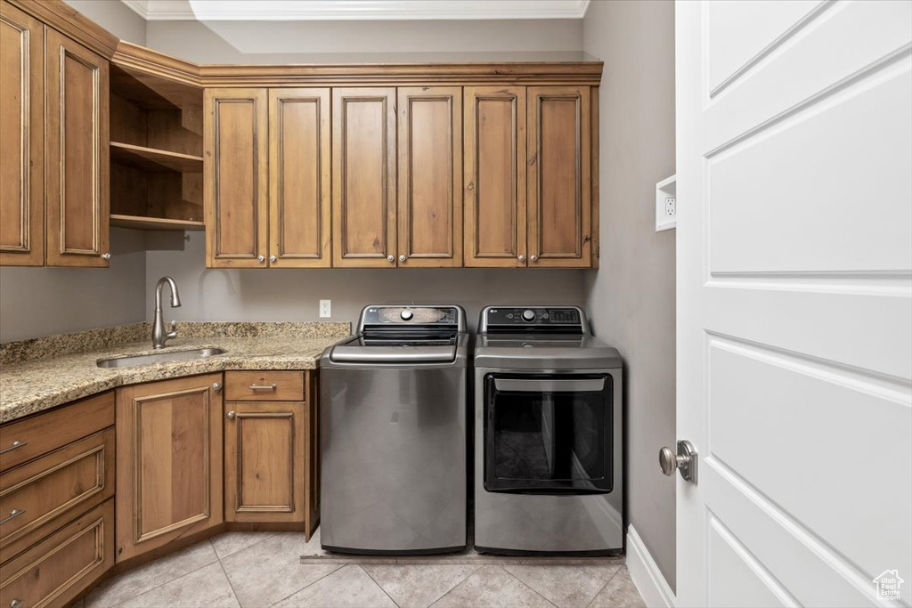 Clothes washing area featuring a sink, cabinet space, light tile patterned flooring, and washing machine and clothes dryer
