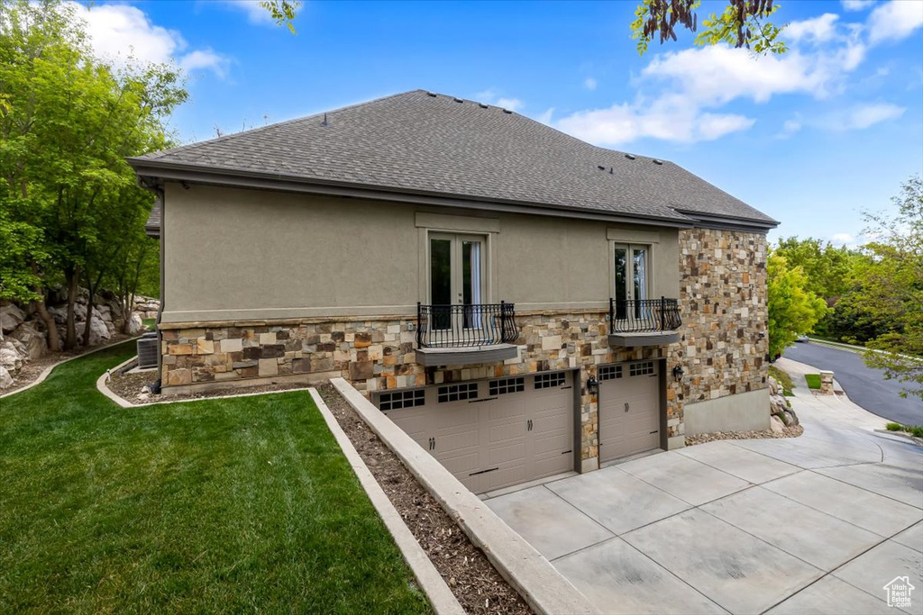 Rear view of property featuring stone siding, stucco siding, roof with shingles, and a balcony