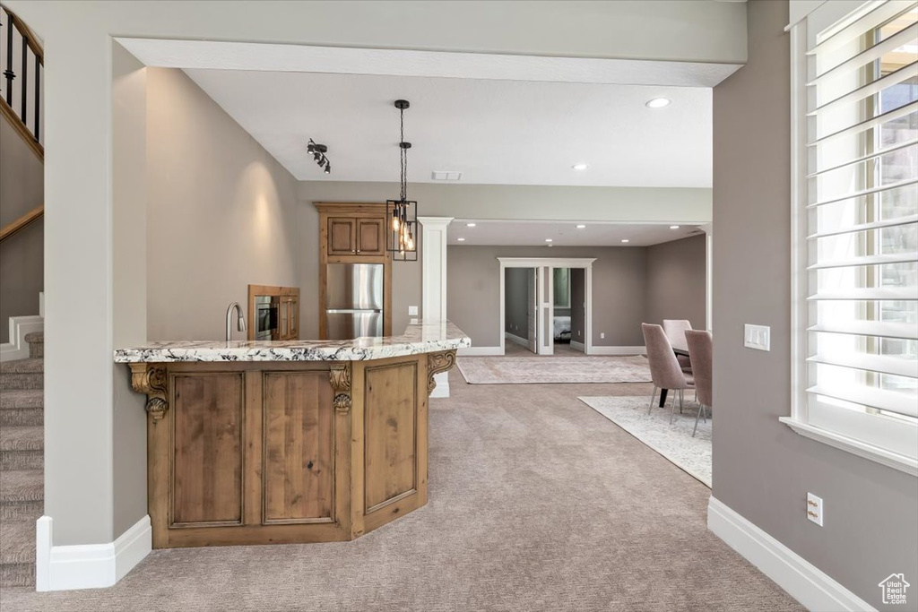 Kitchen featuring a peninsula, brown cabinets, stainless steel refrigerator, light carpet, and light stone counters