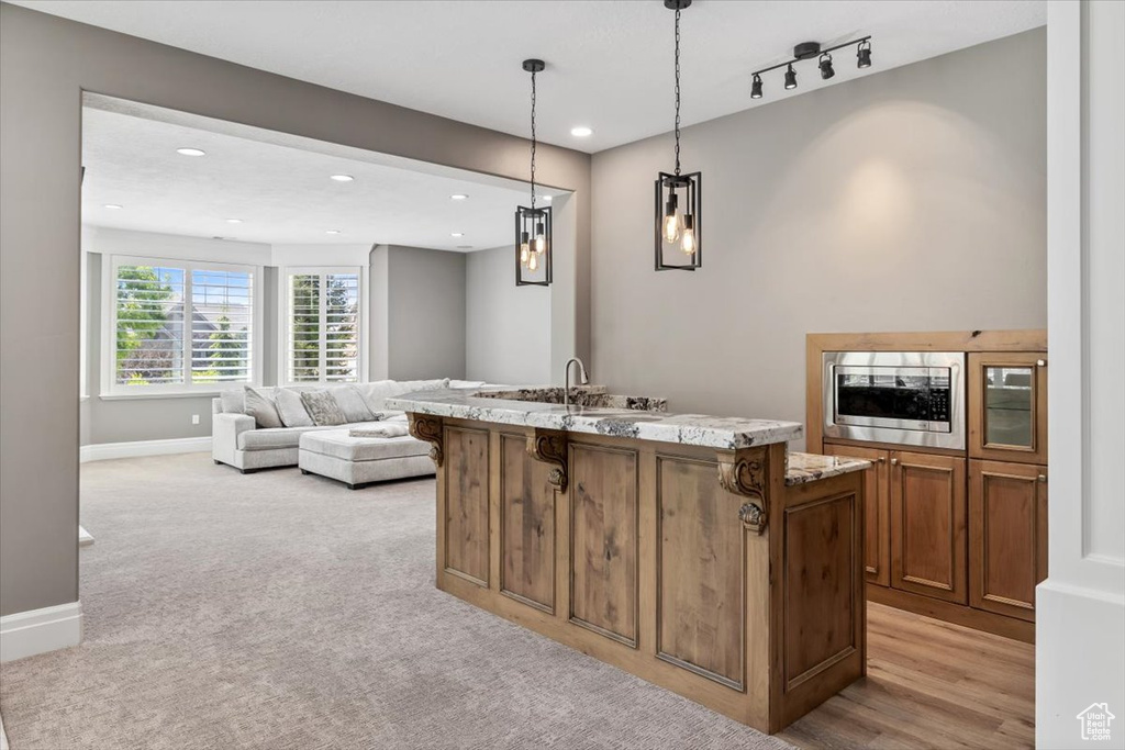 Kitchen with light stone countertops, brown cabinetry, a breakfast bar, stainless steel microwave, and a center island with sink