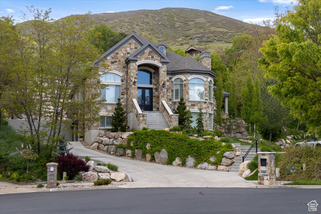 French country home featuring a chimney, french doors, a mountain view, stairs, and stone siding