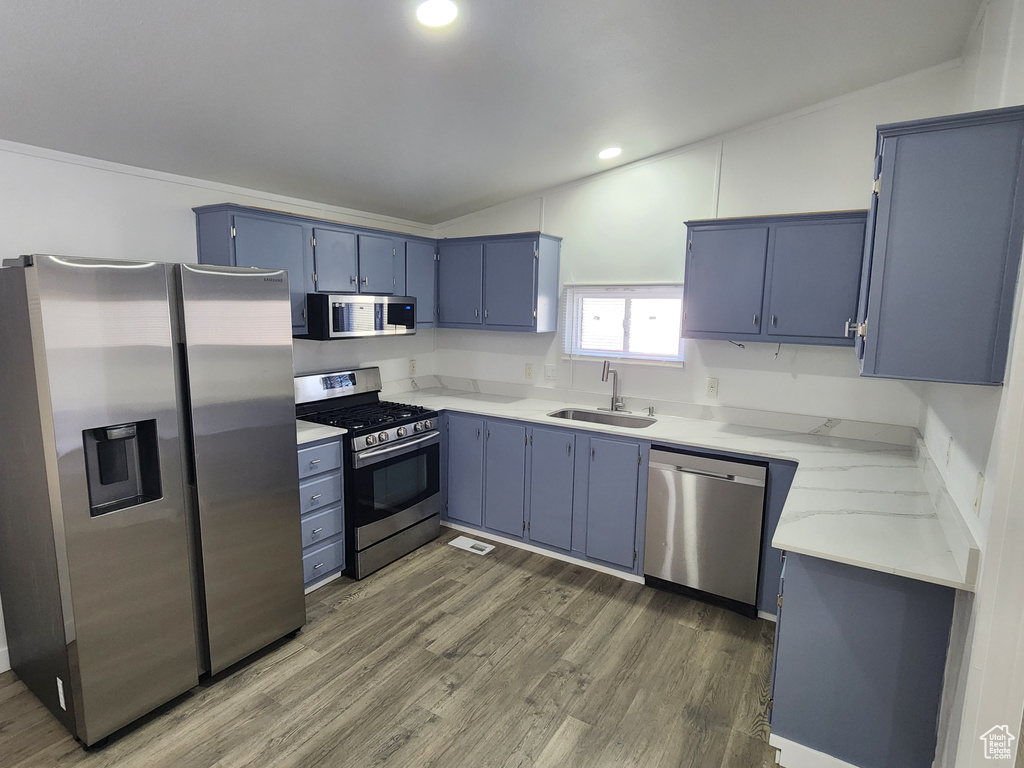 Kitchen featuring a sink, lofted ceiling, stainless steel appliances, wood finished floors, and blue cabinetry