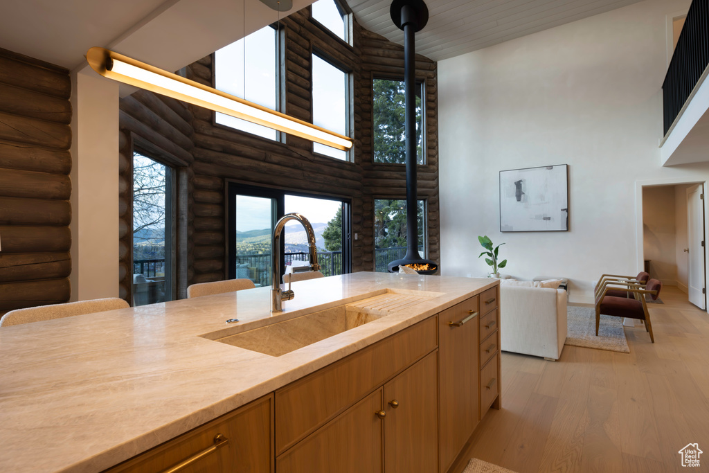 Kitchen with a sink, high vaulted ceiling, light wood finished floors, light countertops, and rustic walls