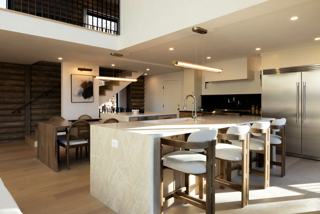Kitchen with a large island, a kitchen bar, stainless steel built in fridge, and light wood-style flooring