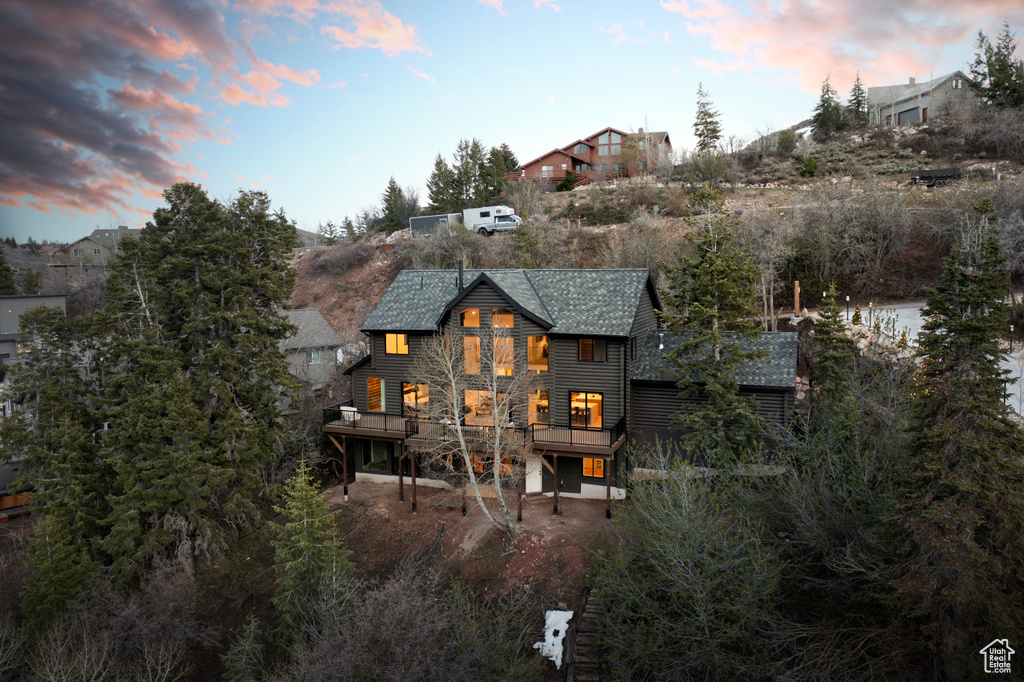 Back of house at dusk with a wooden deck and a shingled roof