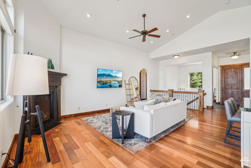 Living area featuring light wood finished floors, a fireplace with flush hearth, arched walkways, ceiling fan, and recessed lighting