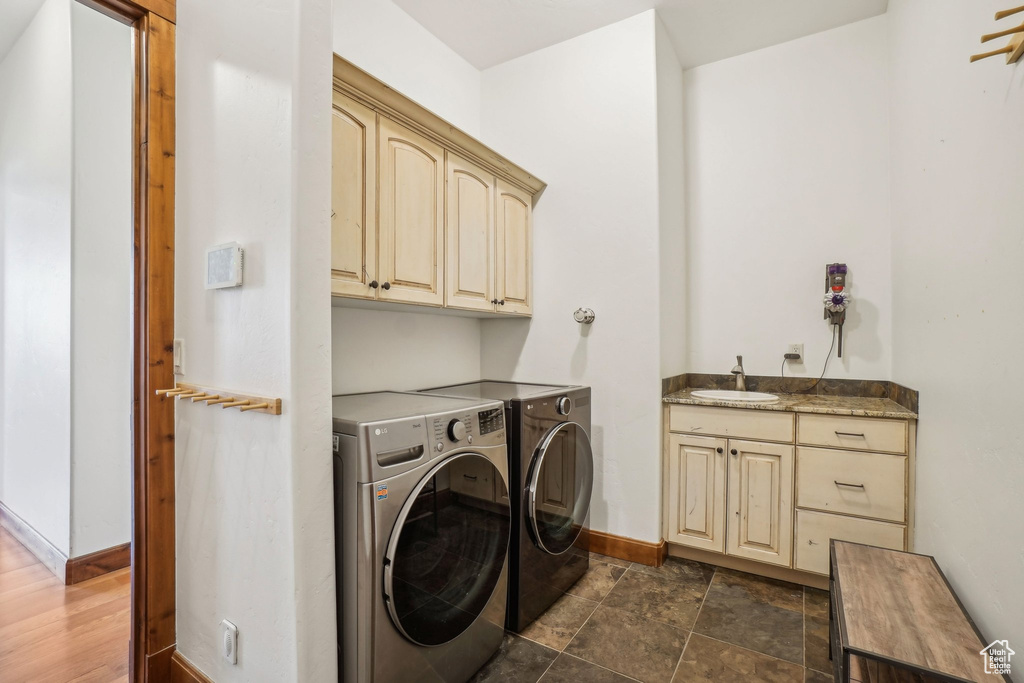 Washroom with cabinet space, washer and clothes dryer, baseboards, and a sink