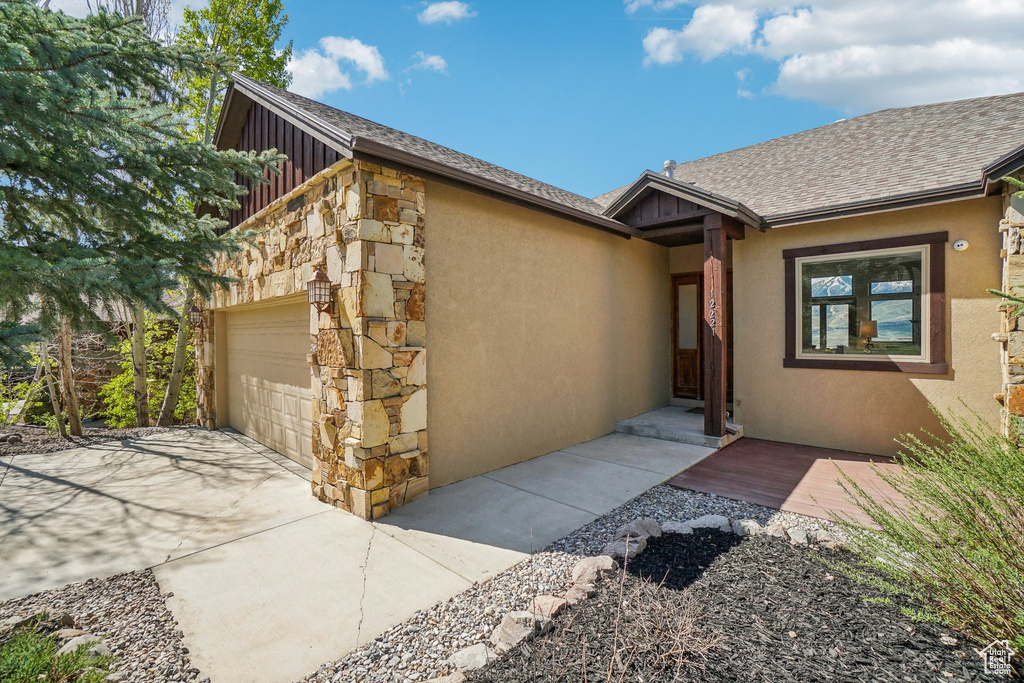 Property entrance with roof with shingles, an attached garage, stone siding, stucco siding, and board and batten siding