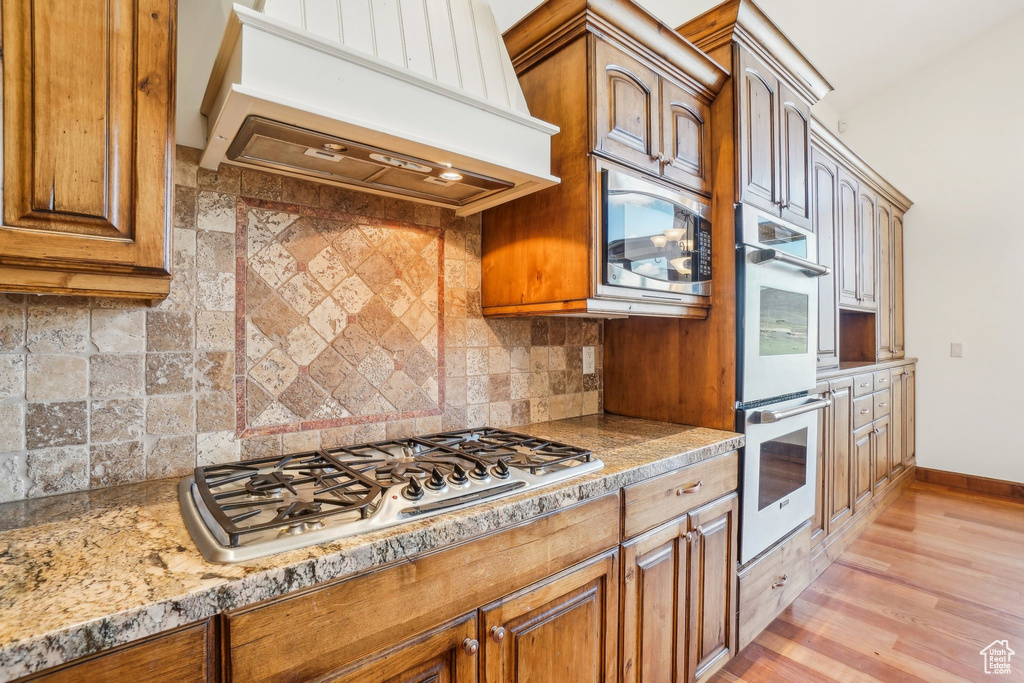 Kitchen featuring brown cabinetry, light wood-style floors, stainless steel appliances, and custom exhaust hood
