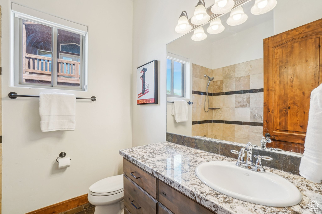 Full bathroom with vanity, toilet, a notable chandelier, and tiled shower