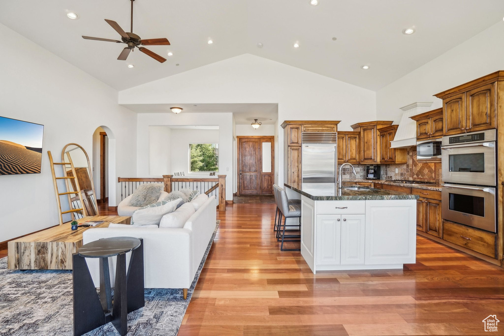 Kitchen with a breakfast bar area, brown cabinetry, open floor plan, light wood-style floors, and appliances with stainless steel finishes