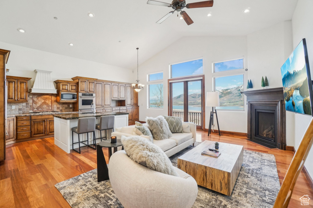 Living area with recessed lighting, ceiling fan with notable chandelier, high vaulted ceiling, a fireplace, and light wood-type flooring