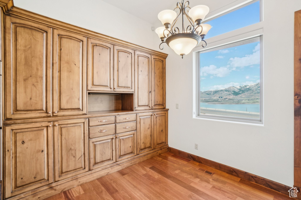 Unfurnished dining area featuring plenty of natural light, light wood-type flooring, a chandelier, and baseboards