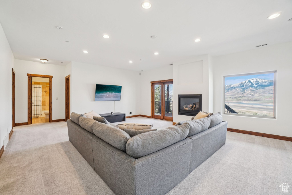 Living room with baseboards, a glass covered fireplace, recessed lighting, and light colored carpet