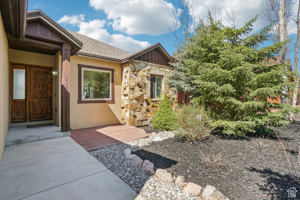 View of exterior entry with stone siding, board and batten siding, stucco siding, and roof with shingles