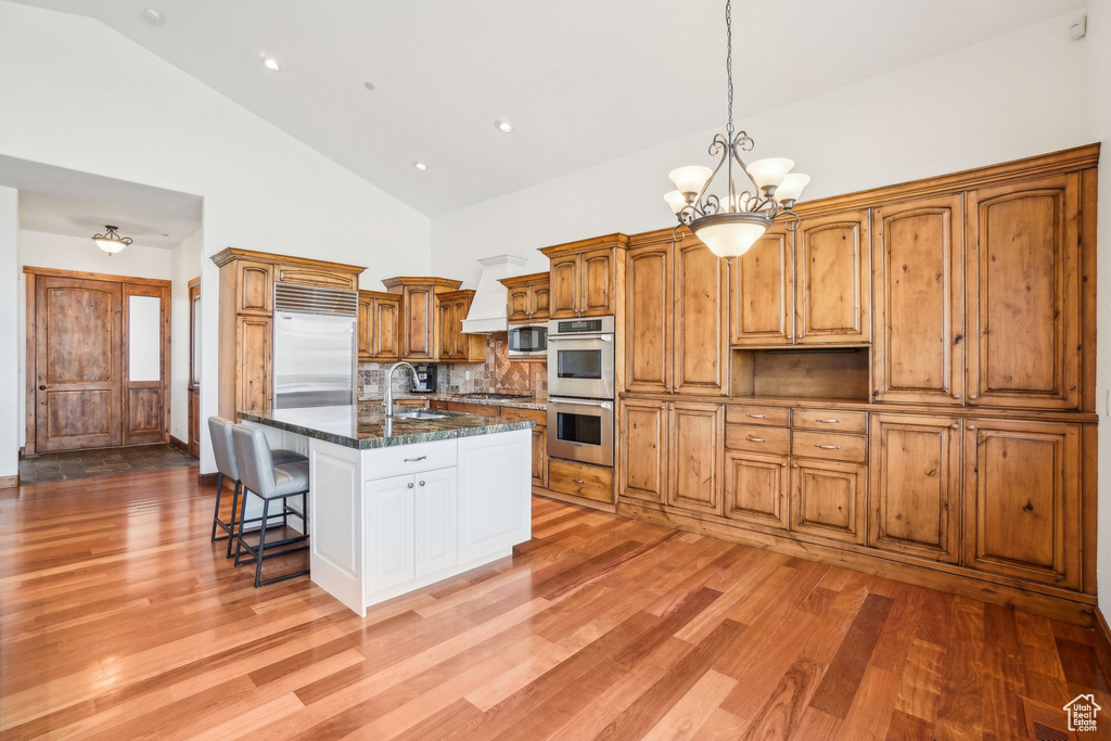 Kitchen with light wood-style flooring, a breakfast bar, high vaulted ceiling, a notable chandelier, and built in appliances