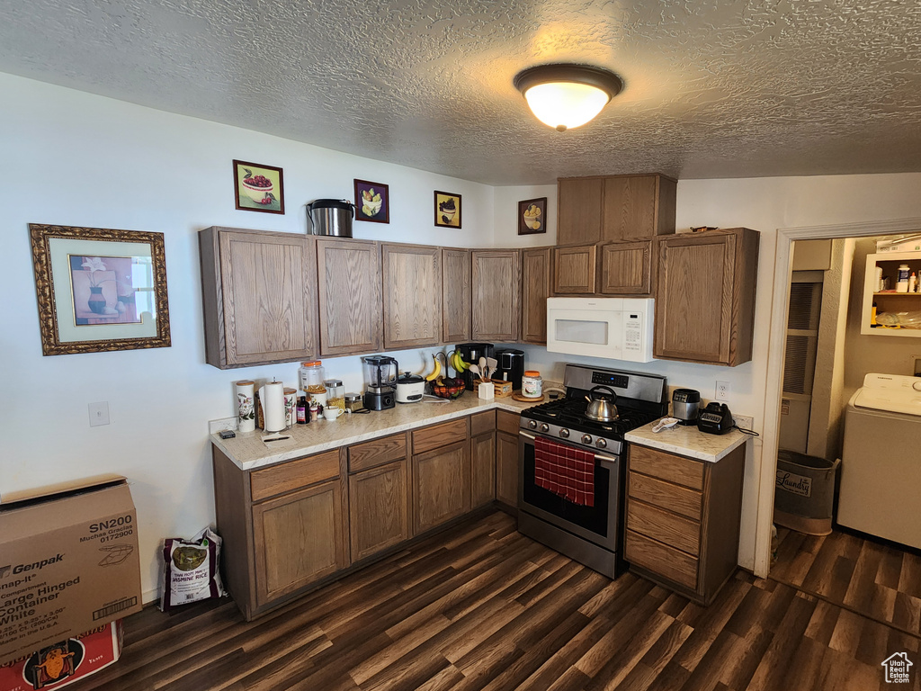 Kitchen featuring washer / clothes dryer, white microwave, dark wood-type flooring, stainless steel range with gas stovetop, and light countertops