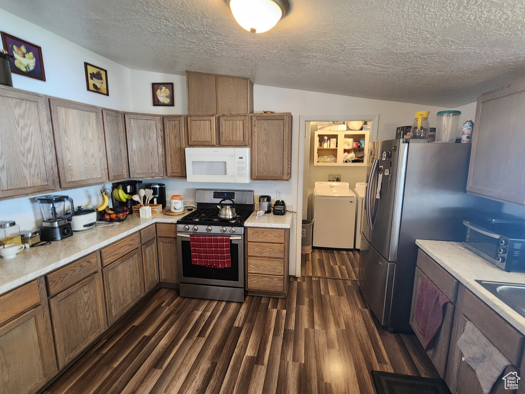 Kitchen with washing machine and dryer, stainless steel appliances, a textured ceiling, dark wood-type flooring, and light countertops