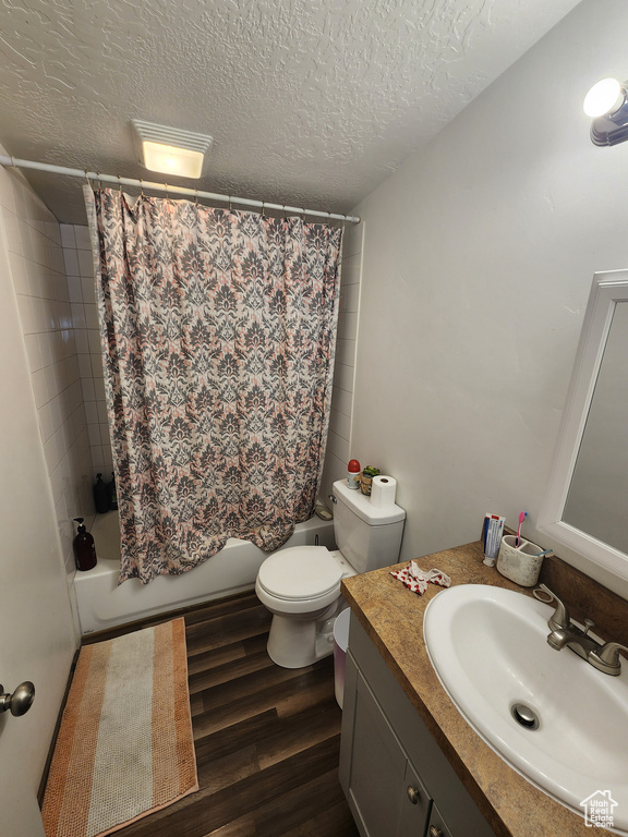 Bathroom featuring toilet, shower / bath combo with shower curtain, wood finished floors, vanity, and a textured ceiling