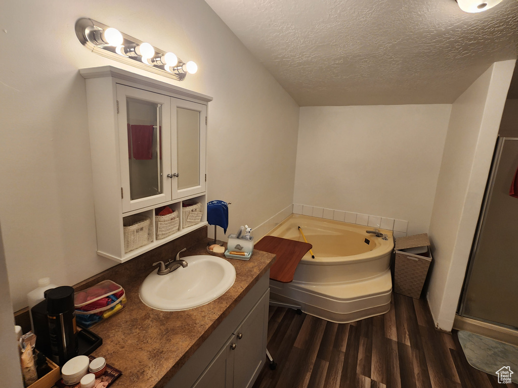 Full bathroom with a garden tub, wood finished floors, a textured ceiling, a shower stall, and vanity